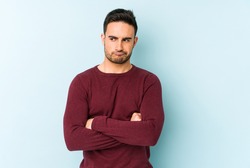 Young caucasian man isolated on blue background frowning face in displeasure, keeps arms folded.