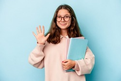 Little caucasian student girl holding books isolated on blue background smiling cheerful showing number five with fingers.