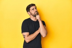 Caucasian man in black t-shirt, yellow studio backdrop thinking and looking up, being reflective, contemplating, having a fantasy.