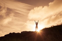 Woman standing on a mountain top with arms in the air celebrating. Victory and winning concept.
