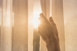 New day concept. Woman's hand opening window curtains early morning with natural light shining through. 