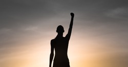 Strong, victorious , and motivated young woman raising her fist up to the sunset sky. Determination and overcoming adversity concept.