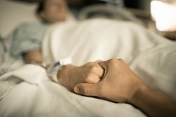 Visitor holding hand of female patient in hospital bed giving support and comfort. 
