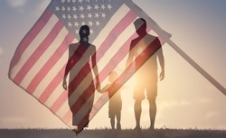Happy family walking together at sunset holding hands agains the flag of America USA background. Double exposure
