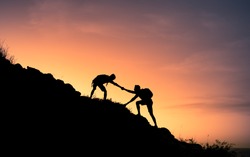 Two male hikers helping each other climb up a mountain. Teamwork and perseverance. 