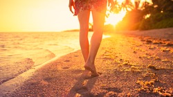 Female walking down a beach during a beautiful golden sunset. Tropical nature getaway concept. 