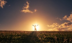 Happy man standing in the sunrise lifting outstretched arms up to the sunset. Mind body and spirit concept. 
