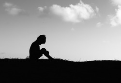 Silhouette of sad little boy child alone sitting with face down. 