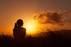 Young woman sitting in a field watching the sunset. 