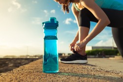 Drinking water concept. Female runner tying her shoe next to bottle of water. 