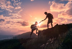 People helping each other hike up a mountain at sunrise.  Giving a helping hand, and active fit lifestyle concept.