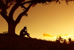 People having problems concept. Silhouette of sad and lonely man sitting alone under a tree. 