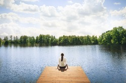 Nature getaway.  Woman sitting on a wooden dock next to lake. 