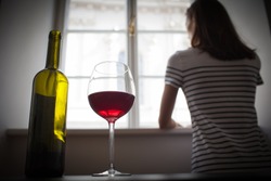 Woman drinking wine alcohol alone looking out her window.  Depression, alcoholism, lonely person concept.  