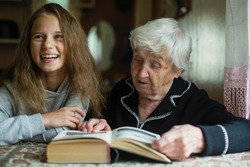 Little cute girl with her old great-grandmother reading a book.