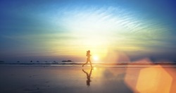  Silhouette of a young girl running along the beach of the sea during an amazing sunset.