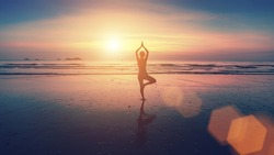 Silhouette of young woman practicing yoga on the beach at beautiful sunset.