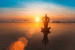 Girl sitting in yoga pose on the beach by the sea at sunset.