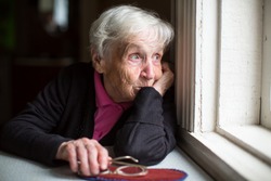 An elderly woman looks sadly out the window.