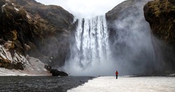 Skogafoss waterfall with solitary person standing near to the flow. Winter scene in southern Iceland. 