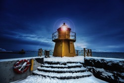 Lighthouse at the entrance to the Old Port, Reykjavik, Iceland. Blue hour shot at dawn during winter, with yellow beacon and snow on the ground. 