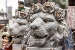 A pair of antique decorative lion head plant pots, with roses forming the mane. Other antiques and bric-a-brac can be seen in the background of a market stall.
