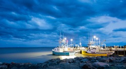 Fishing boats moored in Alma, Bay of Fundy, on the New Brunswick Atlantic coastline in Canada. Blue hour shot with dramatic clouds.