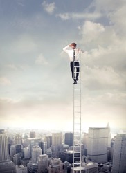 Young businessman  on a ladder over a big city looking ahead