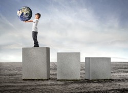 Child holding the earth and standing on the highest of three cubes on a field