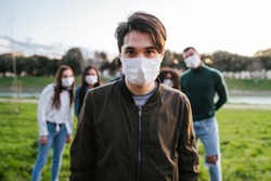 Group of teenagers friends at park wearing medical masks to protect from infections and diseases - Conceptual Coronavirus virus quarantine - Copy space - Multiracial people having fun together