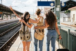 Three young beautiful female women at station to catch train for their vacation together during Coronavirus Covid-19 pandemic wearing protective face masks - Millennials have fun during the holidays