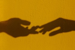 Silhouette of two hands are drawn to each other on a yellow isolated background