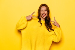 Smiling pretty girl with curly hair winking, showing a tongue, peace gesture. On yellow background.