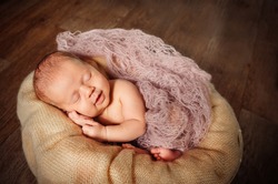 A newborn baby sleeps in a basket on a wooden floor. Beige background. A tender smile of the baby.