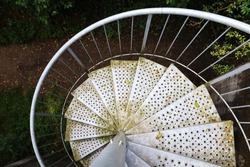 Metal spiral staircase, view from the top down, in the forest. Partially covered with moss, rust and foliage, with perforated sheet. Mystical