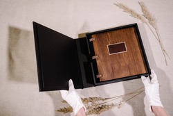 Black case for storing a photo book with a label for the inscription on the cover. The case is opened with white gloves and a photo book with a wooden cover and leather binding is visible inside