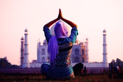 Young christian woman in traditional indian clothes in front of Taj Mahal in Agra, India makes yoga exercises. UNESCO World Heritage Site. Mosque. Mausoleum. Meditation.