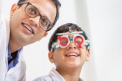 Smiling Indian-thai boy choosing glasses in optics store, Boy doing eye test checking examination with optometrist using trial frame in optical shop