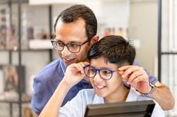Indian father and son choosing eyeglasses in optics store