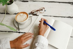  Female hads writing on paper notebook near cup of coffe and glasses. Young woman student writes information from portable net-book while prepare for lectures