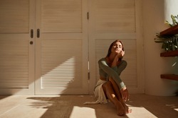 Caucasian model woman sitting on floor and hand cover eyes from the sun near window with strong hard light