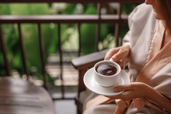 Woman holding cup of hot steaming drink tea on the  balcony with tropical view