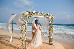 Bride and groom enjoying beach wedding in tropics,  wedding arch, ocean background