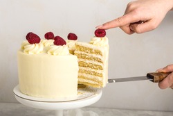 A piece of white cake with cream and raspberry , in a woman's hand, on a metal spatula, grey background.Selective focus.
