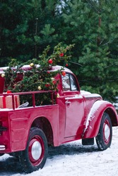 A red car with Christmas decorations and a Christmas tree is standing in a winter forest. Festive New Year concept.