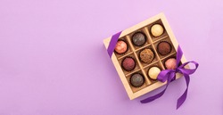 Set of different chocolates in a paper box with a satin purple ribbon on a bright background. Holiday concept.