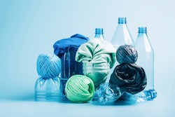 Plastic recycling and reuse concept. Empty plastic bottle and various fabrics made of recycled polyester fiber synthetic fabric on a blue background. Environmental protection waste recycling.