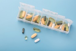 Organizer for pills, vitamins and dietary supplements on a light blue background. Health maintenance concept