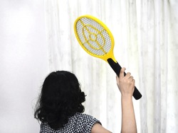 Girl trying to swat mosquitoes with an electronic mosquito racket.