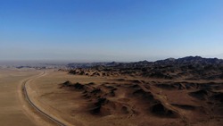 car driving on a gravel path near arid desert mountains.
Aerial view from drones empty road and mountains. Vast wide open desert landscape with dirt roads. Clay Mountains